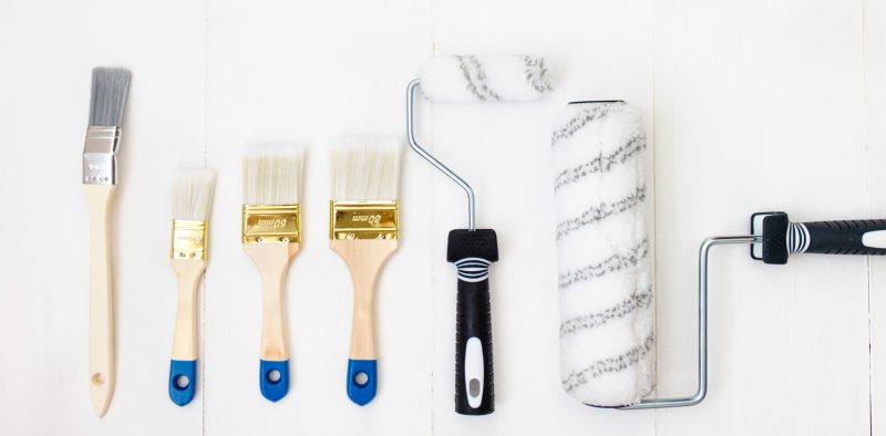 Paint brush, sponge roller, paints on white wooden planks, top view. Decoratng supplies.